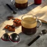 Чашка кофе Nespresso, шоколад, капсулы на столе.