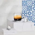 Кофе в стеклянной кружке рядом с капсулами